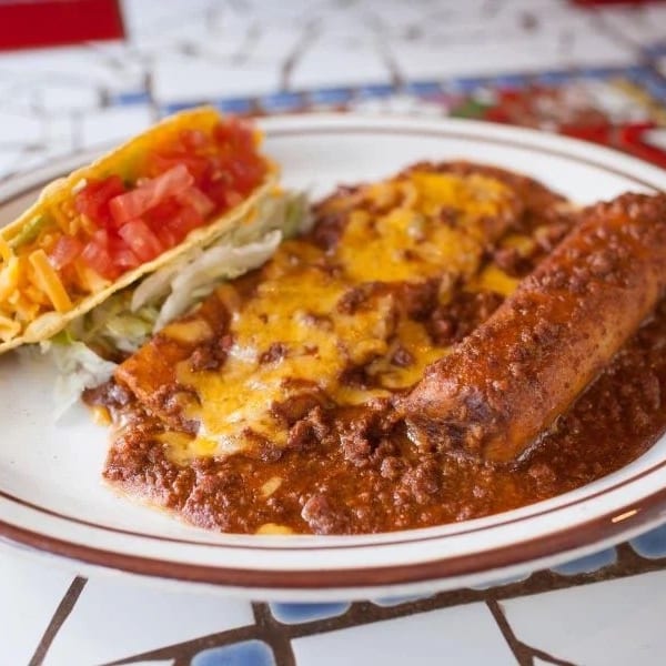 A plate of Mexican food with a taco, enchilada, and chili con carne.