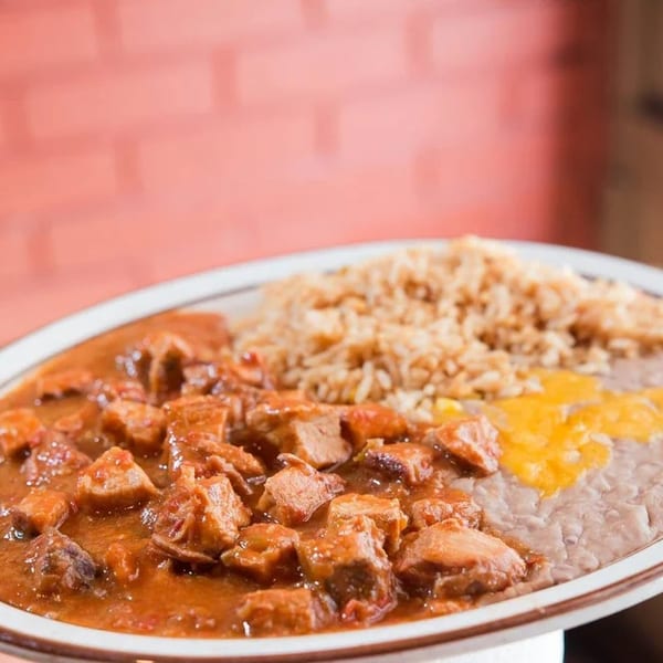 A plate of chili Colorado with rice and refried beans topped with melted cheese.
