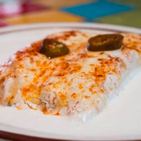 A close-up of a cheesy enchilada topped with two jalapeño slices and red spice.
