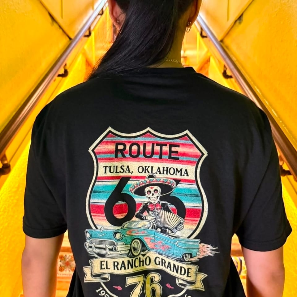 Person wearing an El Rancho Grande Route 66 T-shirt stands in a brightly painted yellow stairway.