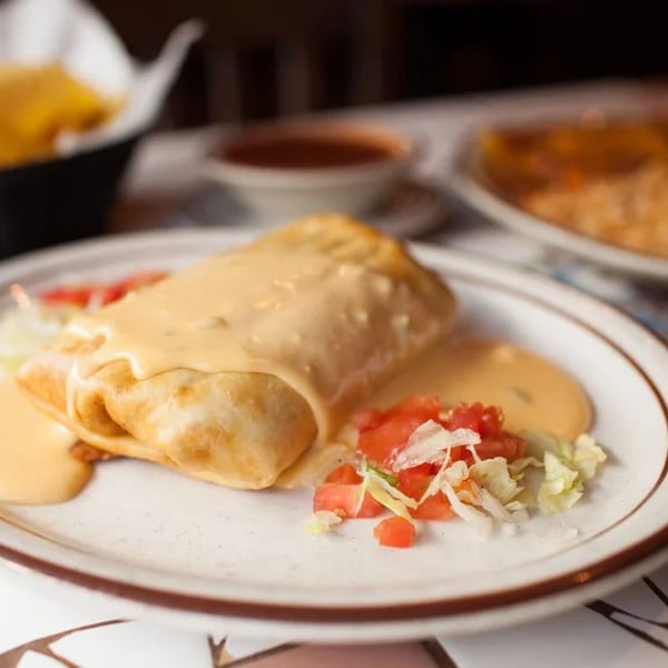 Golden-brown chimichanga smothered in queso, served with diced tomatoes and shredded lettuce.