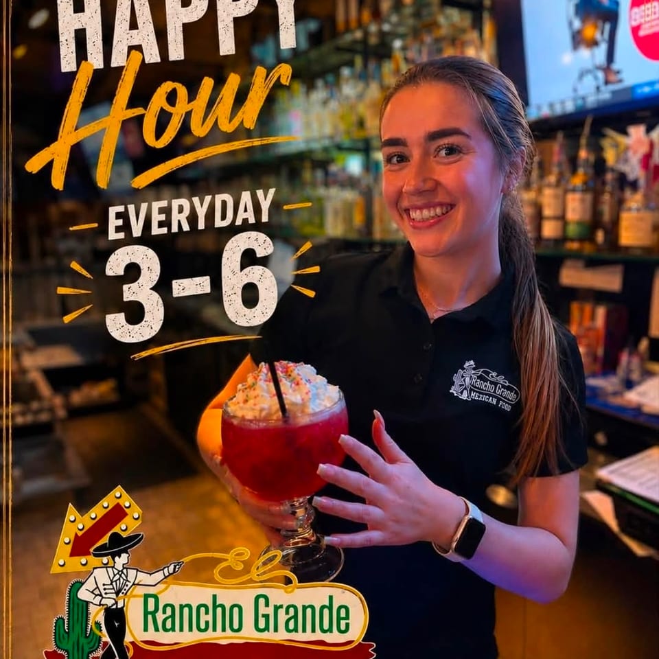 Smiling Rancho Grande server holds a colorful frozen cocktail inside the warmly lit Mexican restaurant during daily 3–6 happy hour.