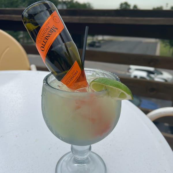 A Mionetto Prosecco bottle inverted into a margarita glass with a lime wedge on a white table.