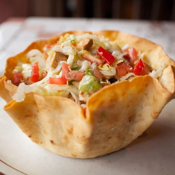 A taco salad in a crispy fried tortilla bowl, filled with lettuce, tomatoes, and chicken.