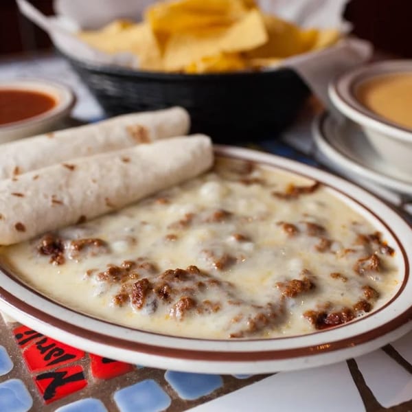 Queso fundido with tortillas, salsa, and a bowl of queso dip on a mosaic table.