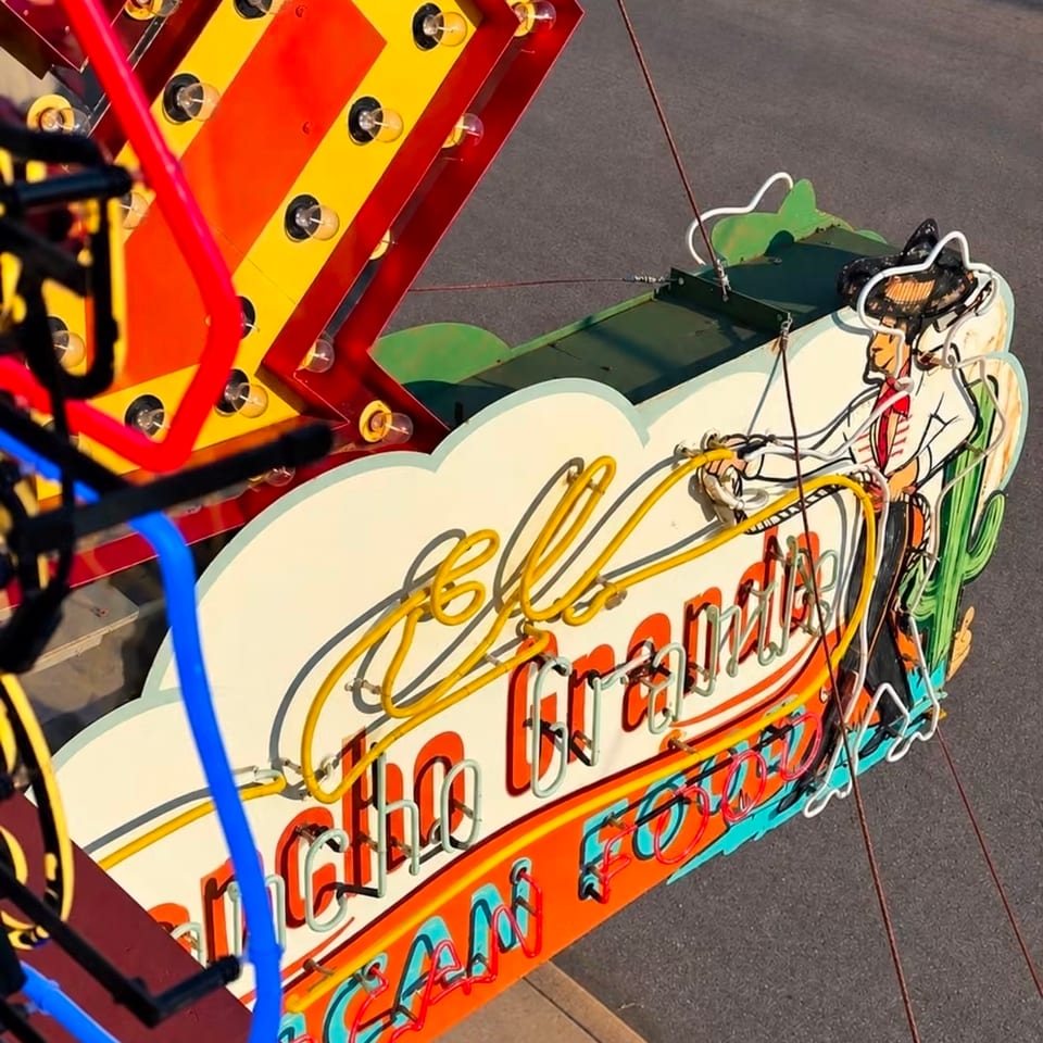 Colorful retro neon restaurant sign featuring marquee bulbs, an illustrated cowboy, and layered red, yellow, blue, and green lettering.