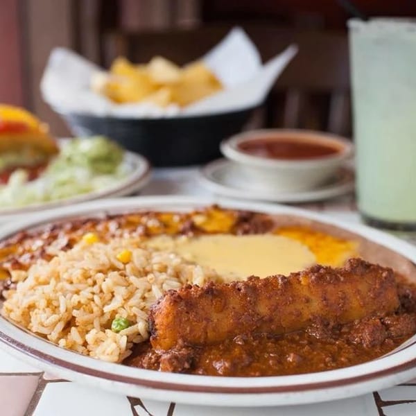 A plate of Mexican food with rice, beans, and a chile relleno, alongside a taco and margarita.