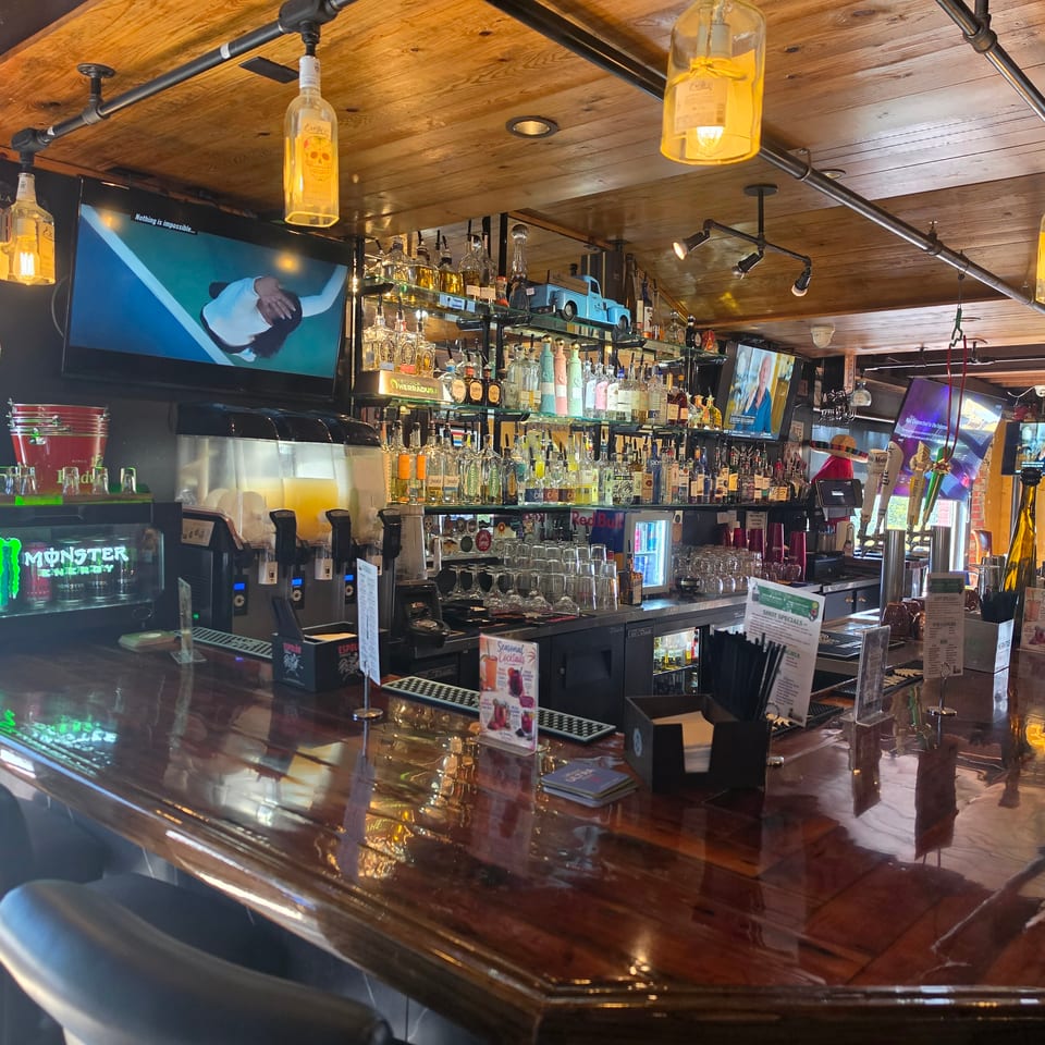 Rustic tequila bar with liquor shelves, glowing bottle lamps, beer taps, televisions, and a polished wooden counter.