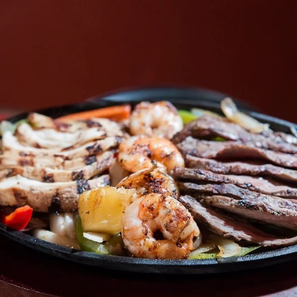 Sizzling fajitas with grilled chicken, steak, shrimp, and vegetables on a cast iron platter.
