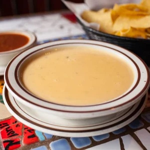 Creamy queso, salsa, and tortilla chips served on a vibrant mosaic table.