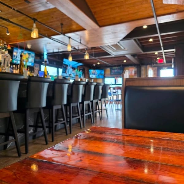 Warmly lit restaurant interior with a glossy wooden table in the foreground and a bar area in the background.