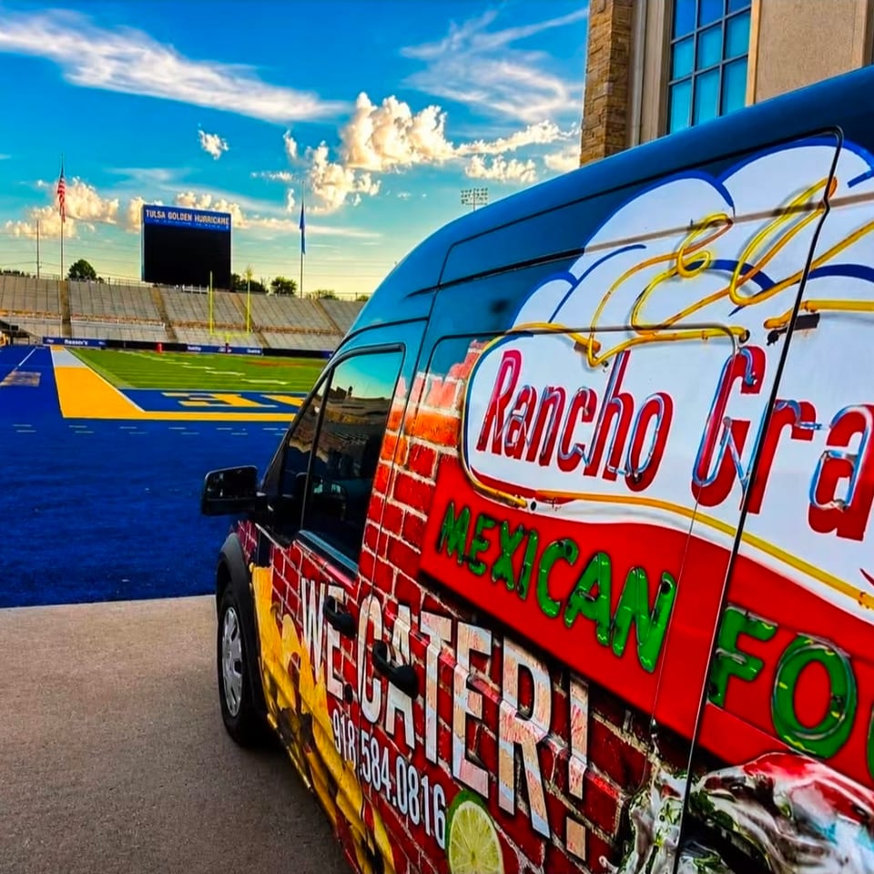 Colorful Rancho Grande Mexican food truck parked beside a blue football field at Tulsa Golden Hurricane Stadium.