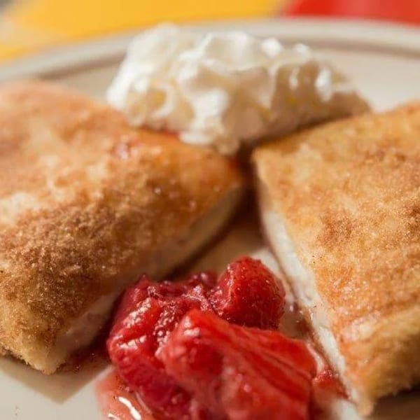 Two golden-brown fried pastries, dusted with cinnamon sugar, served with whipped cream and strawberries.