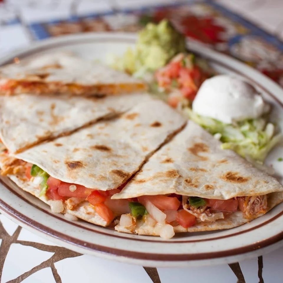 Plate of grilled quesadillas filled with vegetables and meat, served with guacamole, salsa, sour cream, and lettuce.