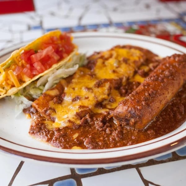 A plate of Mexican food with a taco, enchiladas, and a tamale covered in chili and cheese.