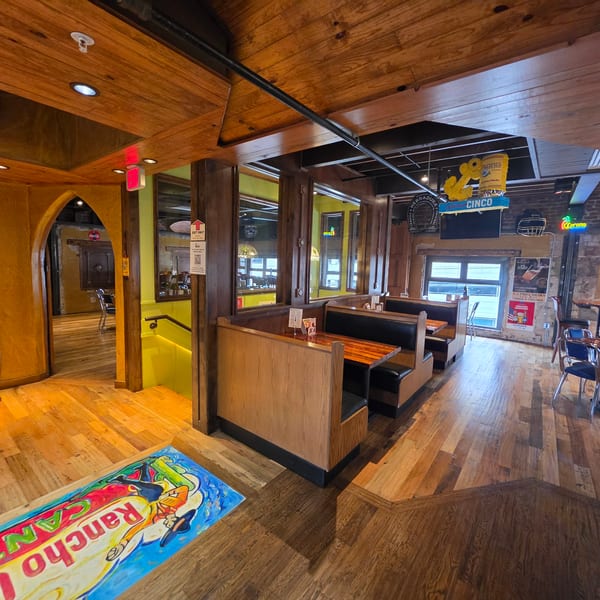 Rustic Mexican restaurant dining room with wooden booths, colorful floor mural, exposed brick, and beer-themed decorations.