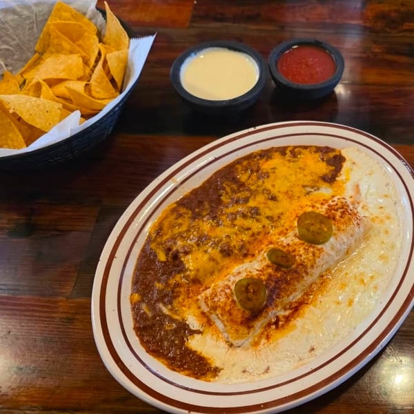 Burrito covered in red and white sauce with jalapeños, alongside chips, queso, and salsa.