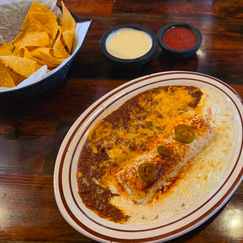 Burrito covered in red and white sauce with jalapeños, alongside chips, queso, and salsa.