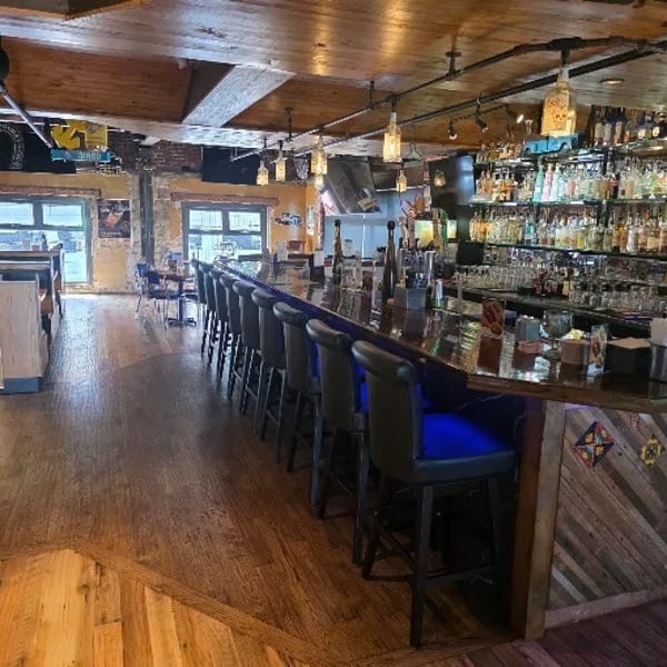 A long, well-stocked bar with stools and booths in a restaurant with wooden floors and exposed beams.