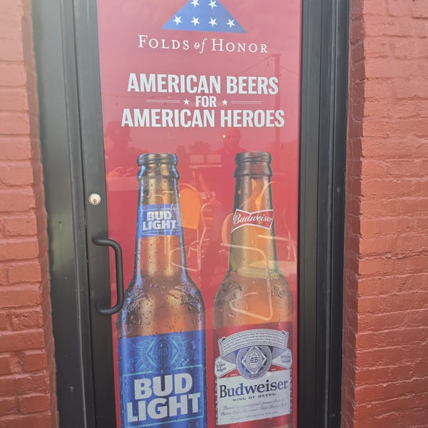 Restaurant door displays a patriotic Bud Light and Budweiser poster reading “Folds of Honor: American Beers for American Heroes.”
