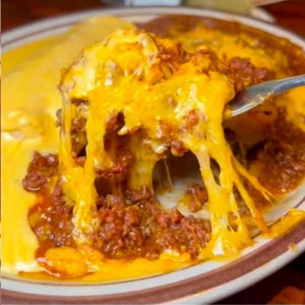 Fork lifting a cheesy, meaty enchilada, with melted cheese stretching from the plate.