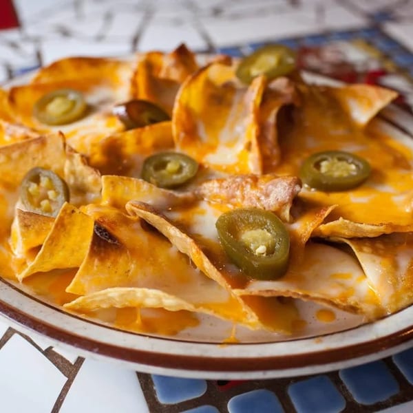 A plate of cheesy nachos topped with sliced jalapeños on a mosaic table.