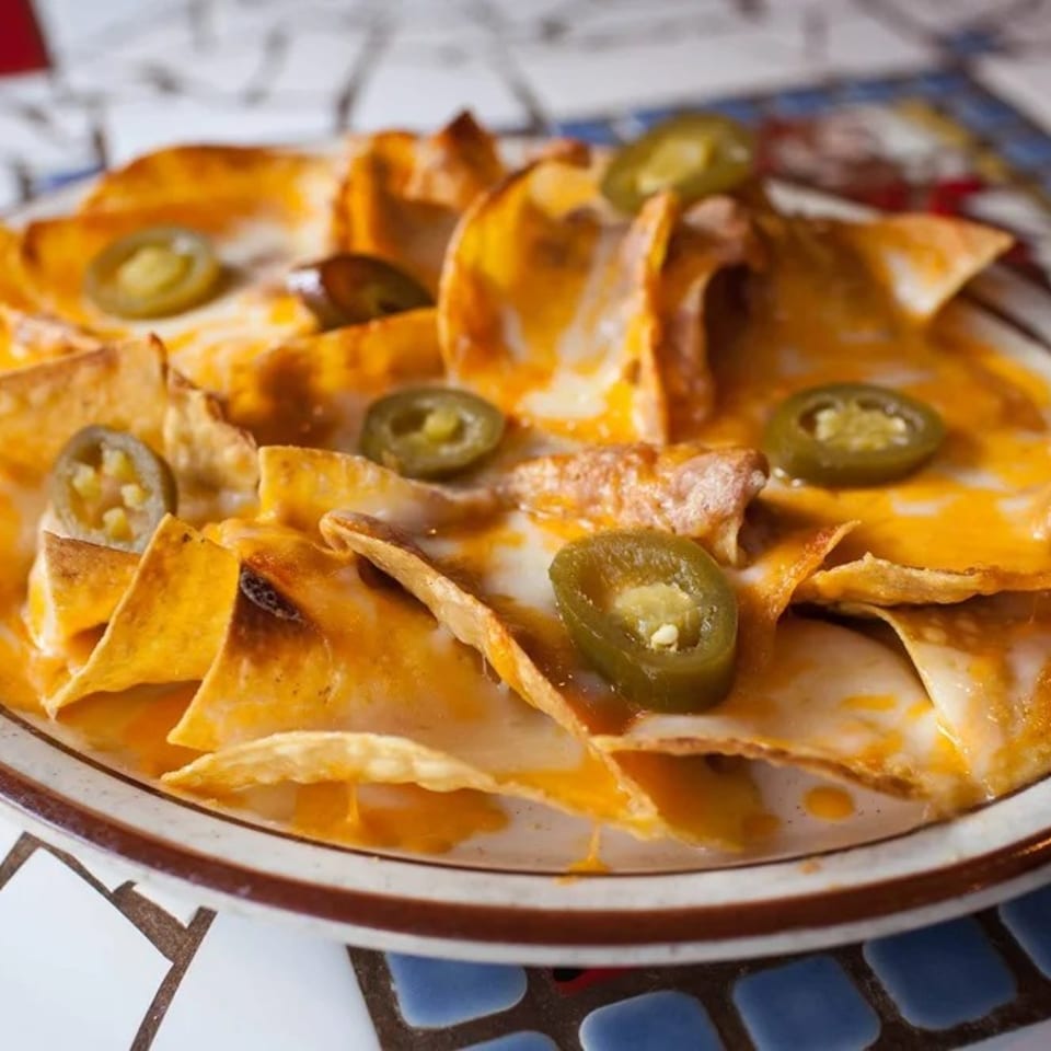 A plate of cheesy nachos topped with sliced jalapeños on a mosaic table.