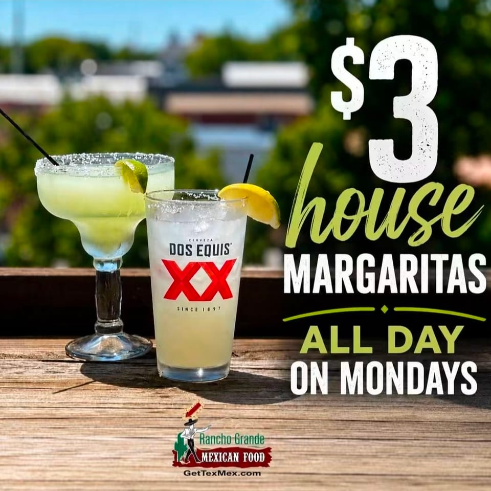 Two lime-garnished margaritas sit on a wooden table beside promotional text for Rancho Grande Mexican Food’s all-day Monday margaritas.