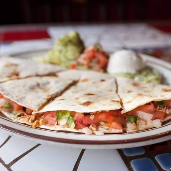 Chicken quesadillas with diced tomatoes, onions, and lettuce, served with guacamole and sour cream.