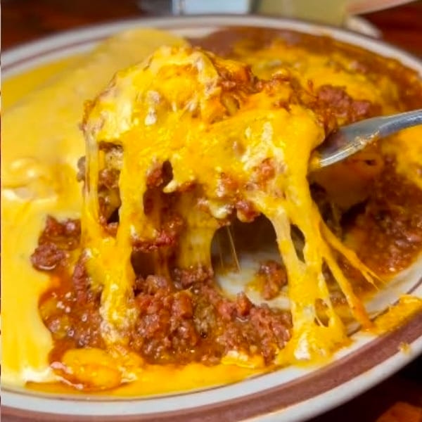 Fork lifting cheesy baked pasta layered with seasoned ground meat, melted cheese stretching over a ceramic plate.