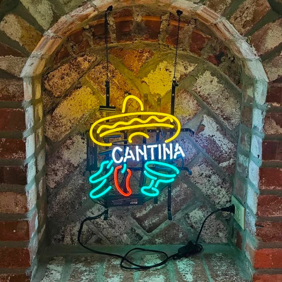 Colorful neon Cantina sign featuring a sombrero, chili peppers, and cocktail glasses mounted in a rustic brick archway.