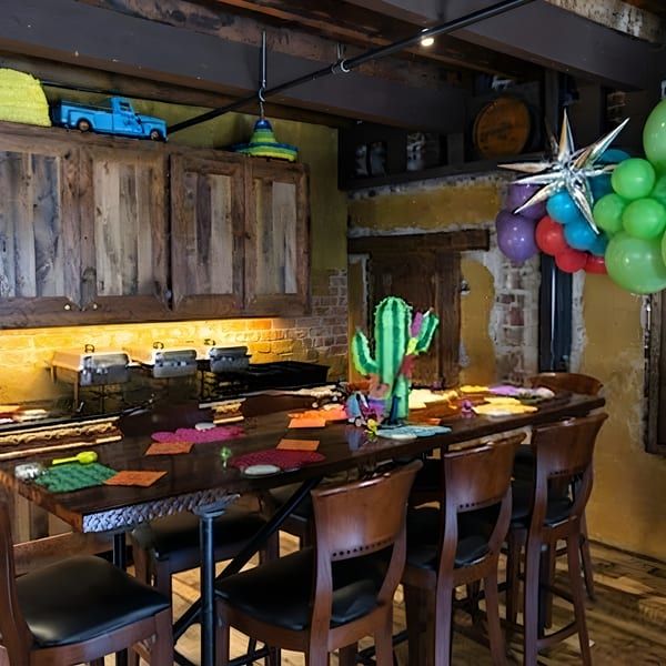 A vibrant restaurant interior with a long wooden table, bar stools, and festive Mexican decorations.