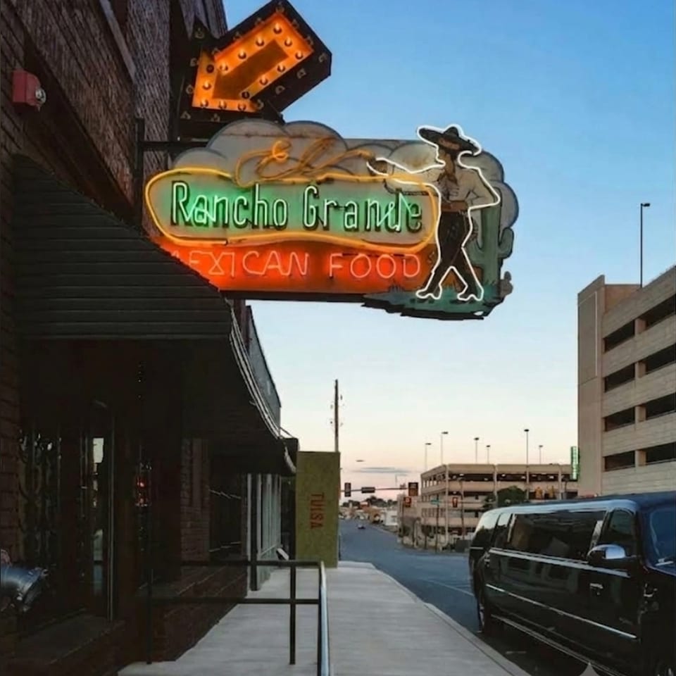Neon Rancho Grande Mexican Food sign with a dancing figure outside a brick restaurant on a city sidewalk.