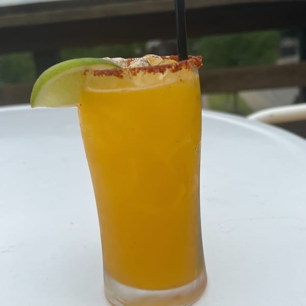 A vibrant orange drink with a lime wedge and chili-salt rim sits on a white table outdoors.